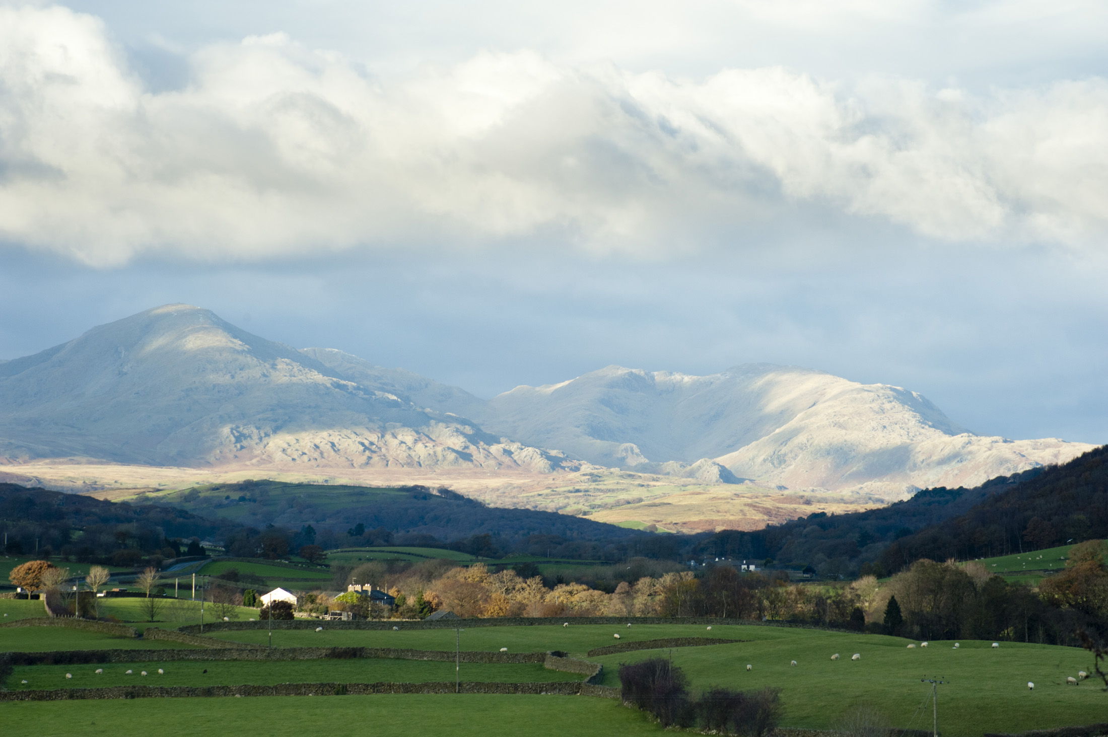 an image of Scenic landscape in the English Lake District with a view of lush green pastiures and farm buildings below a mountain range