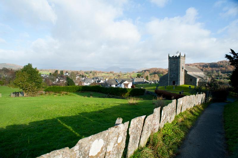 View across an old stone wall and lush green pasture of the picturesque village of Hawkshead in the Cumbrian Lake District, a popular tourist destination