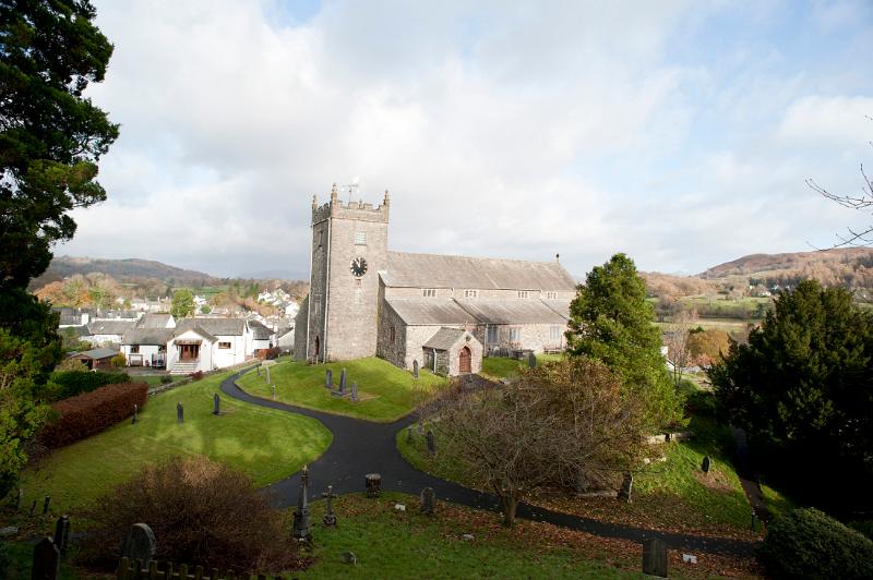 Picturesque view between trees of the Hawkshead stone church and village in the Lake District in Cumbria with rolling hills behind