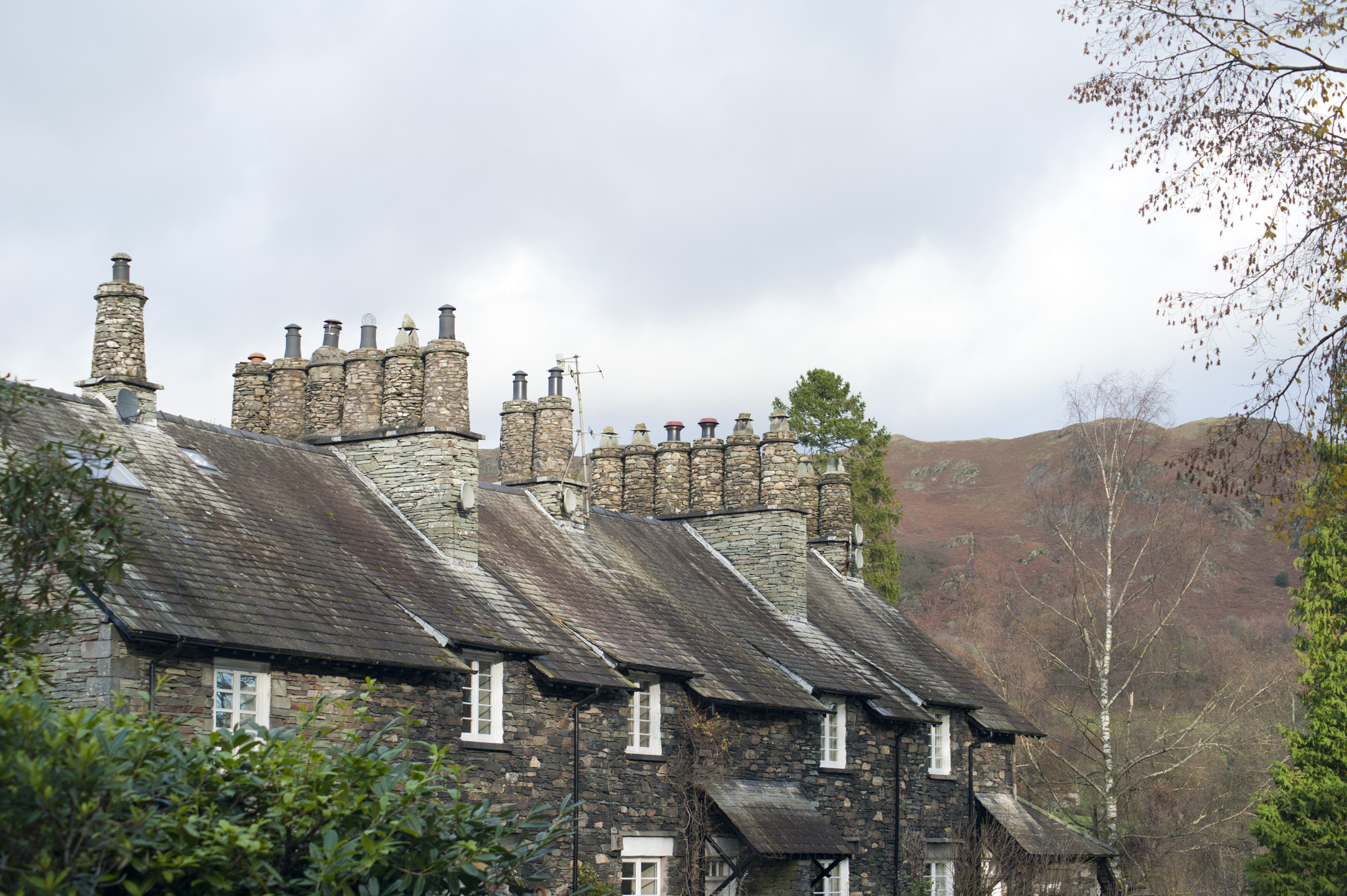 an image of Row of quaint stone cottages at Skelwith Bridge in the Lake District with traditional cylindrical chimney pots made of stone in a leafy green lane