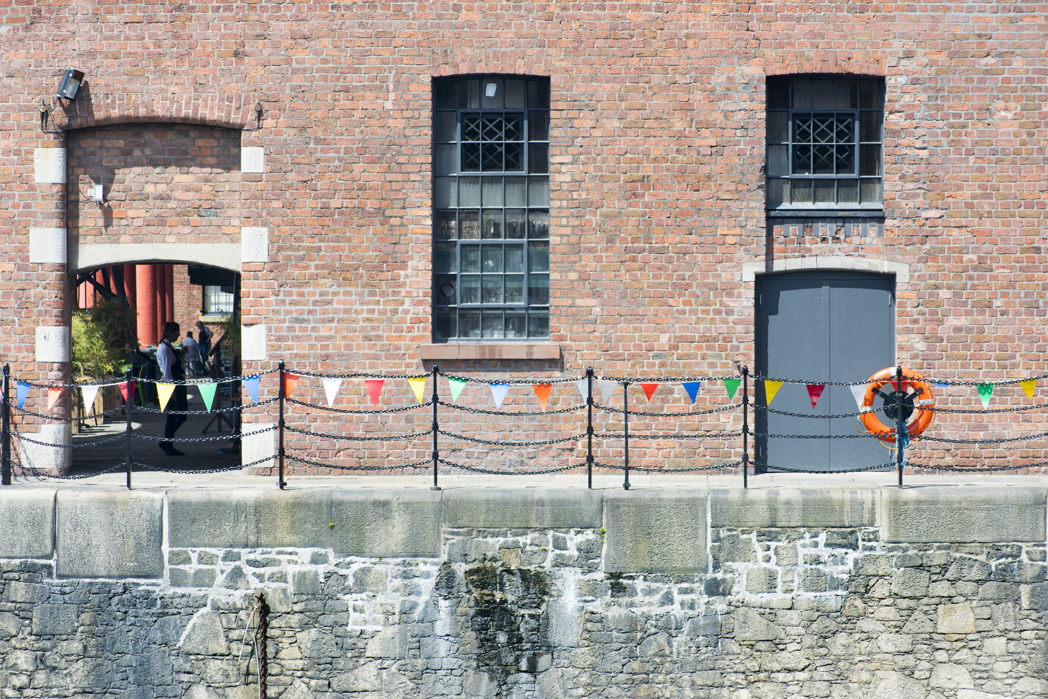 an image of Brick wall with railings at foreground with windows and doors above stone wall with copy space at Liverpool Albert Dock