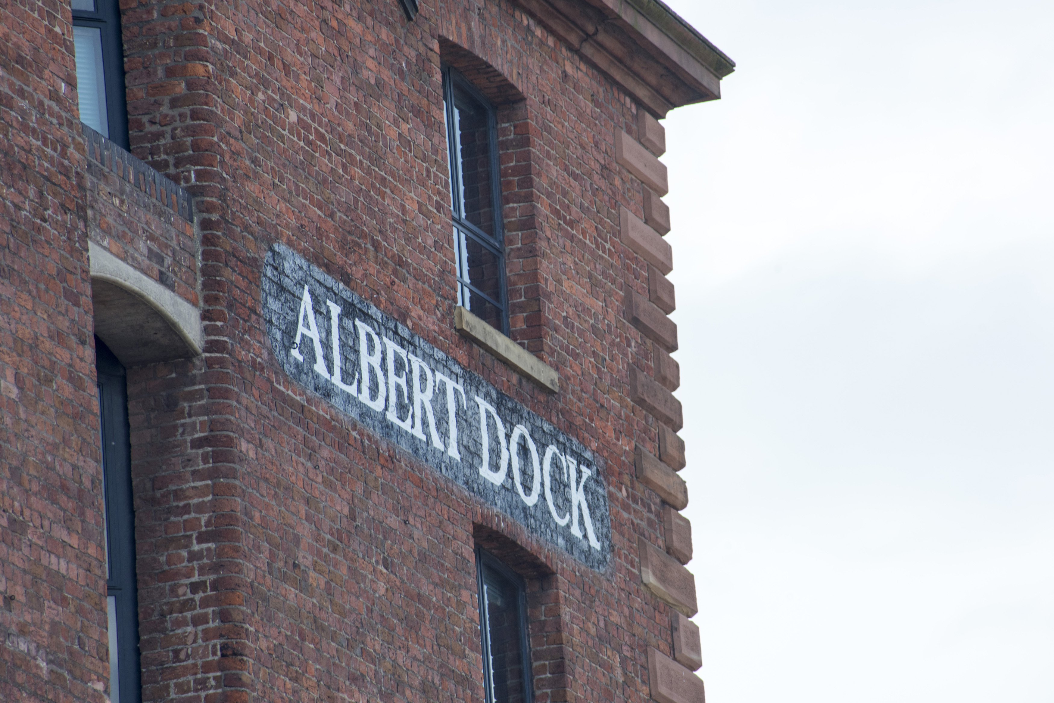 an image of Detail on Albert Dock painted brick sign in between windows in Liverpool with over cast sky