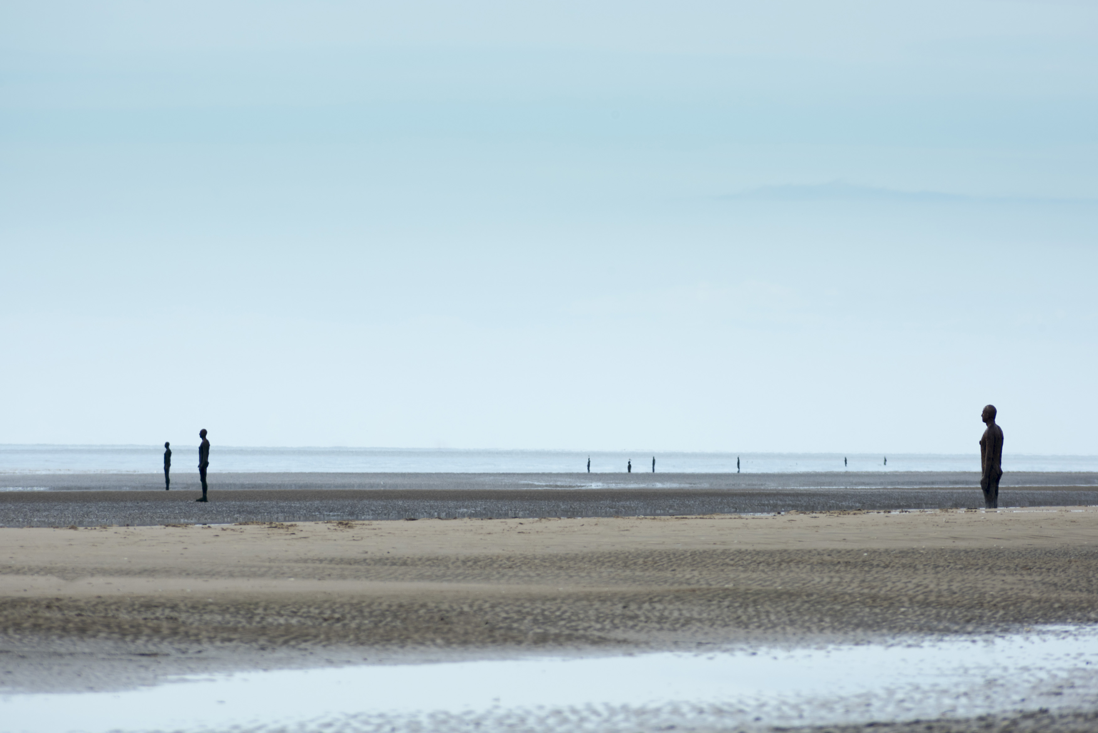 an image of Another Place sculptures on the beach at Crosby, United Kingdom under overcast sky with copy space