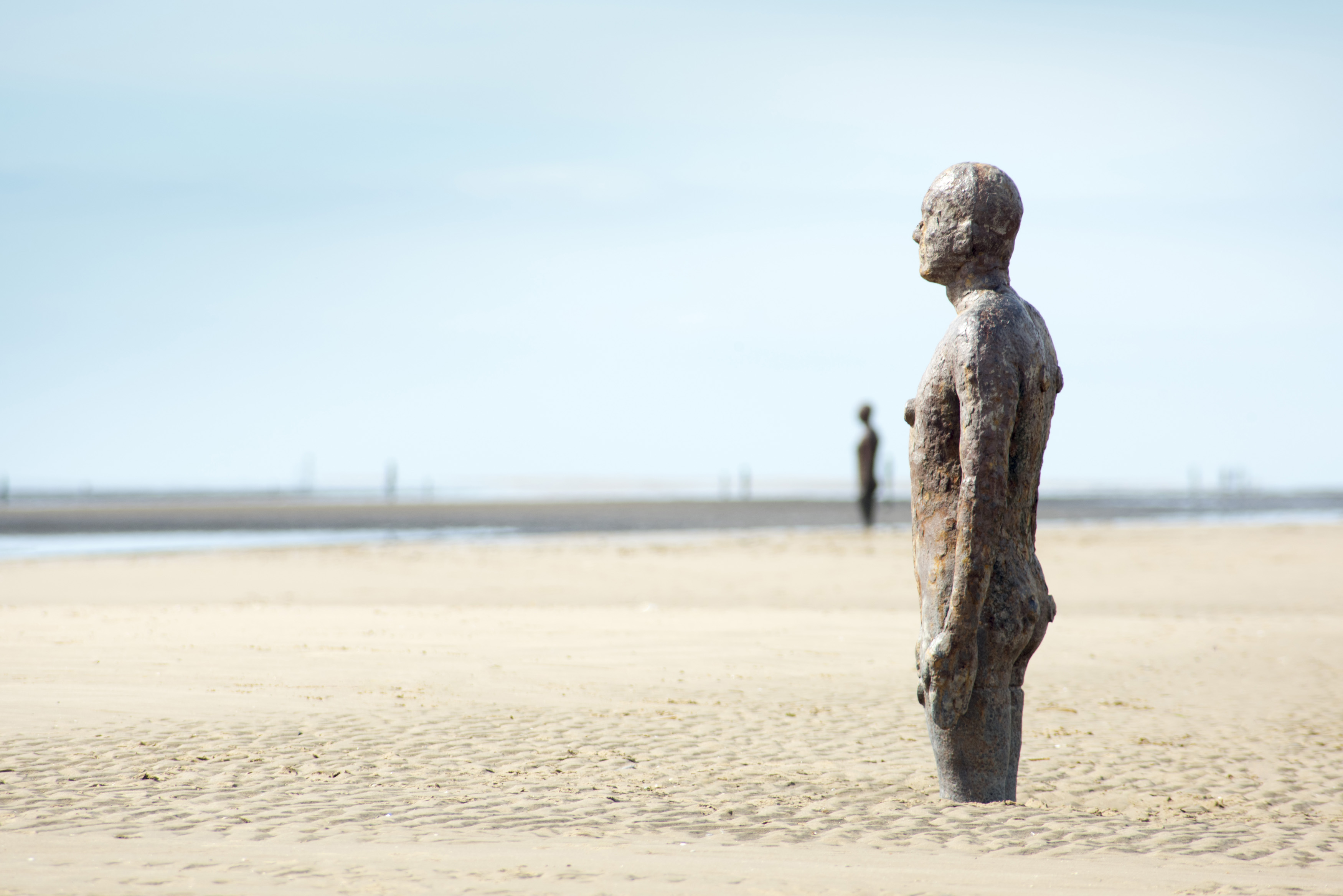 an image of Cast iron statue in the sand on a beach facing out to sea - Another Place, by Antony Gormley at Crosby Beach, Liverpool UK
