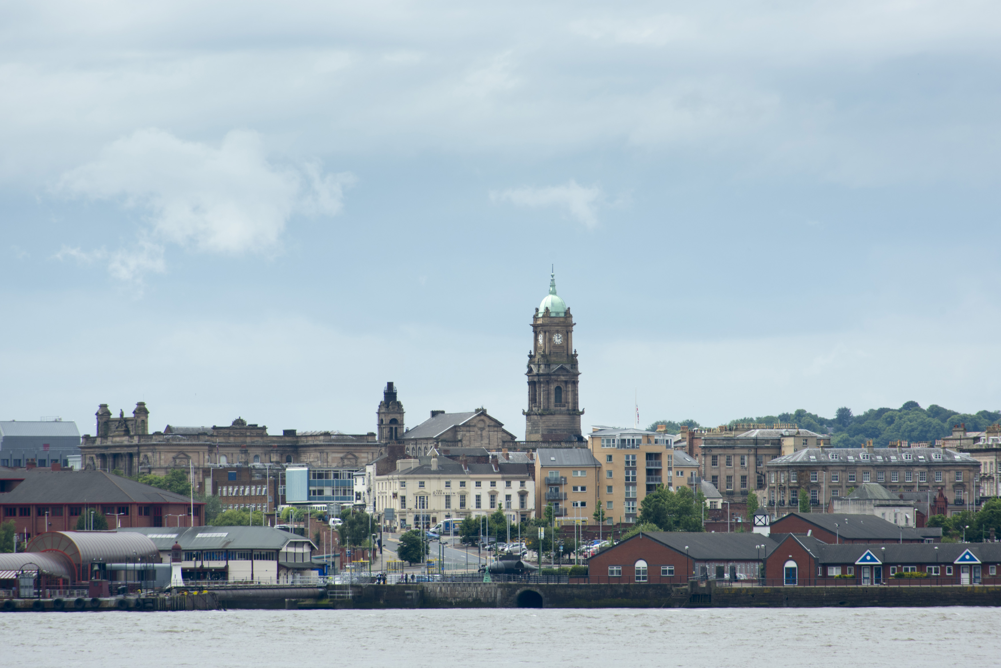 an image of Empty waterfront shoreline seen from Liverpool across the Mersey with various famous landmark buildings and docks under cloudy sky