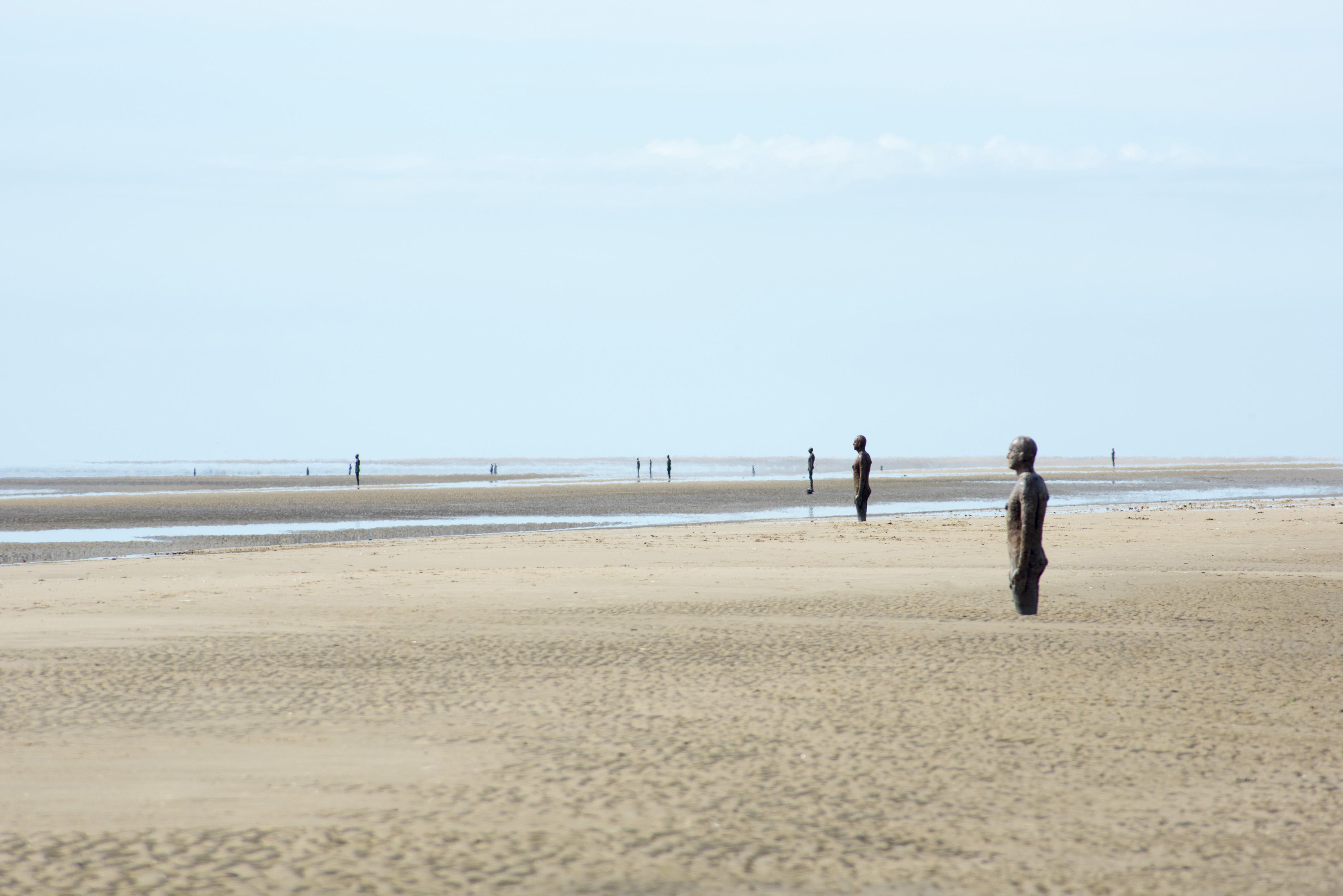 an image of Another Place by Antony Gormley, Crosby Beach, Liverpool with 100 cast iron statues standing facing out towards the ocean
