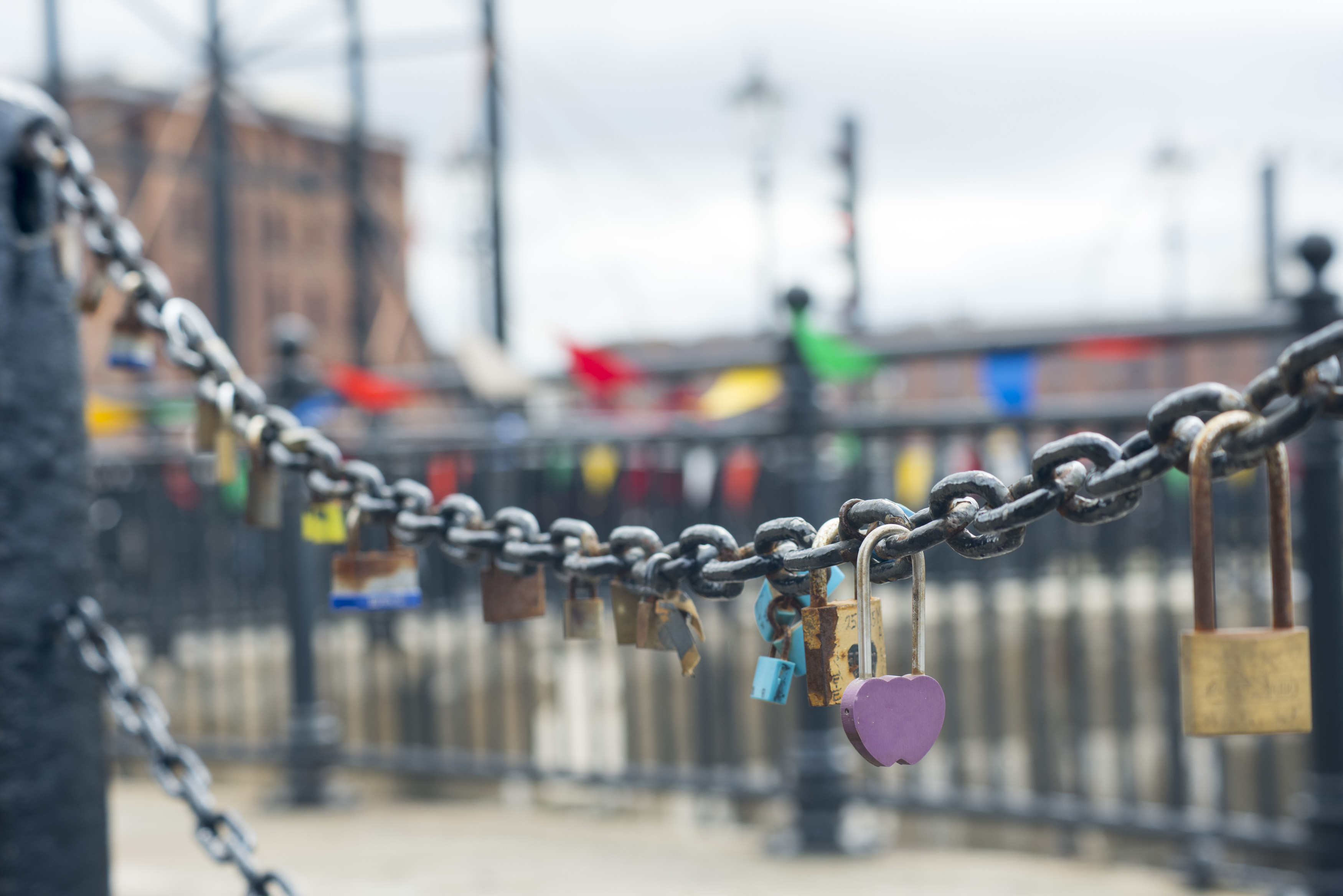 an image of Various unique padlocks on old chain railing in Liverpool at the Mersey Waterfront outdoors