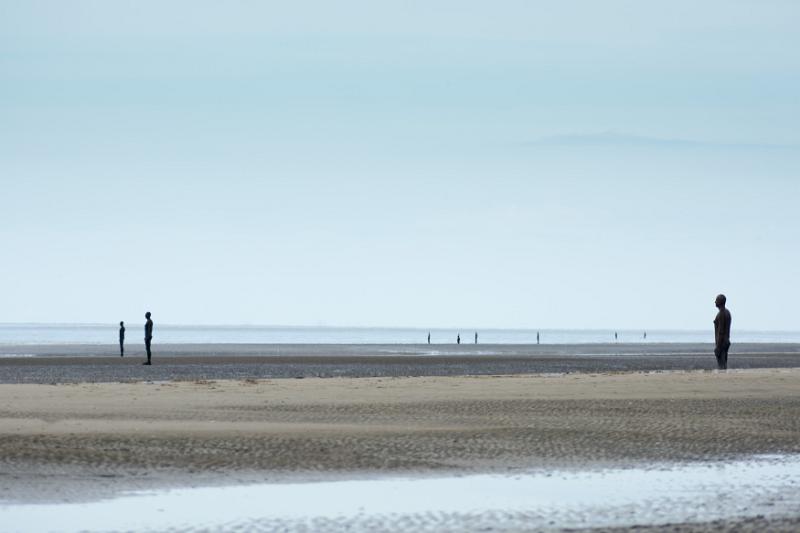 Another Place sculptures on the beach at Crosby, United Kingdom under overcast sky with copy space