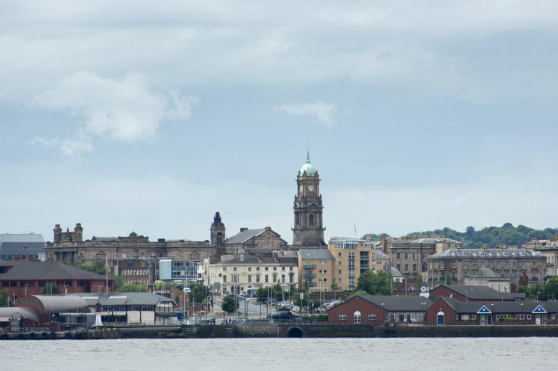 Empty waterfront shoreline seen from Liverpool across the Mersey with various famous landmark buildings and docks under cloudy sky