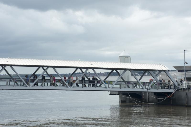 Various unidentifiable tourists traveling across a covered pedestrian walkway bridge over water in Liverpool