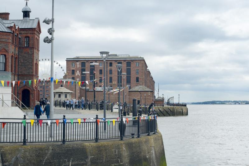 Various tourists walking around landmark buildings near round railing along waterfront at Liverpool Mersey