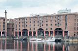 View from across the bay of three small boats docked at Liverpool Albert Dock in front of brick building with red columns