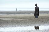 Pair of human shaped standing sculptures partially covered in sand at Crosby, UK under overcast sky