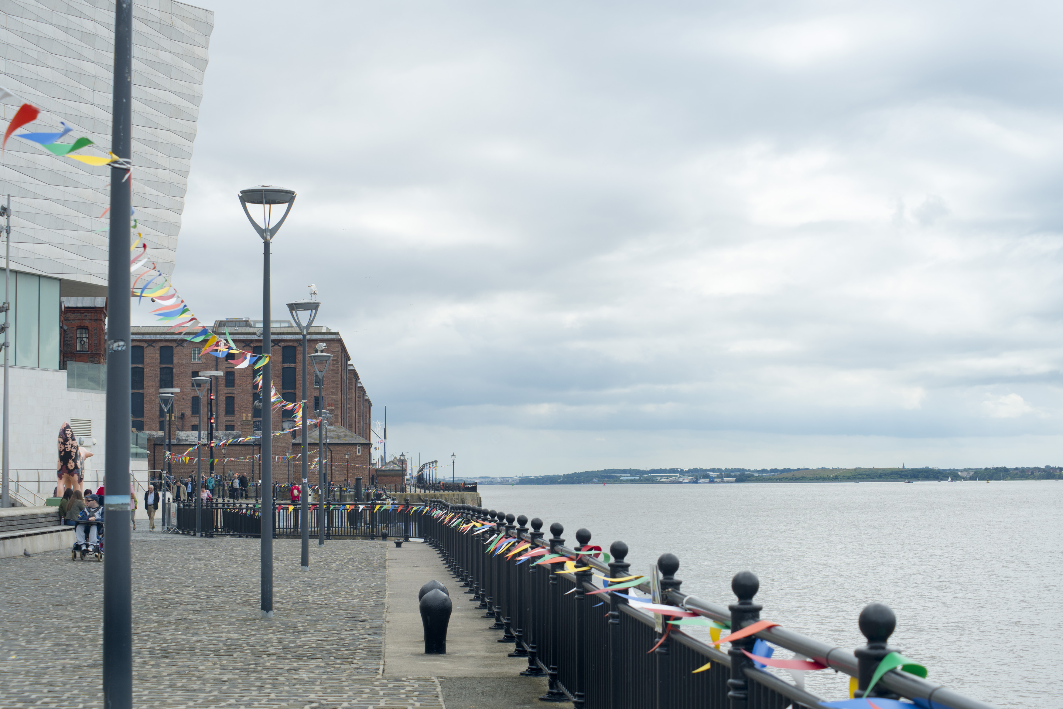 an image of Cobbled promenade at Liverpool Mersey waterfront with colorful bunting on the street lamps and railing leading to the historical buildings in the background, Liverpool, England