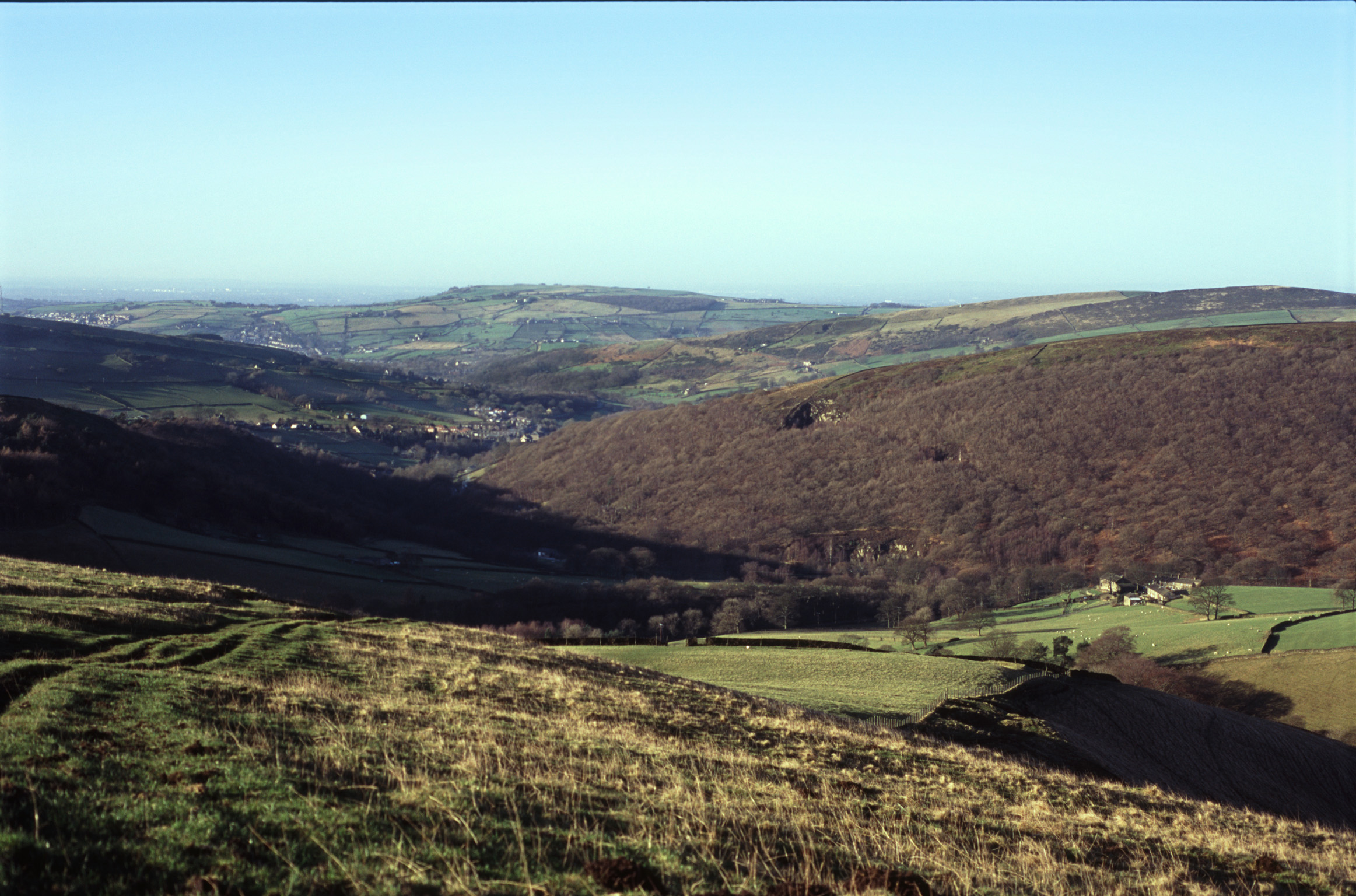 an image of View across the Kinder Scout moor land with its rolling hills, grassland and pasture on a sunny clear blue sky day, Derbyshire, UK
