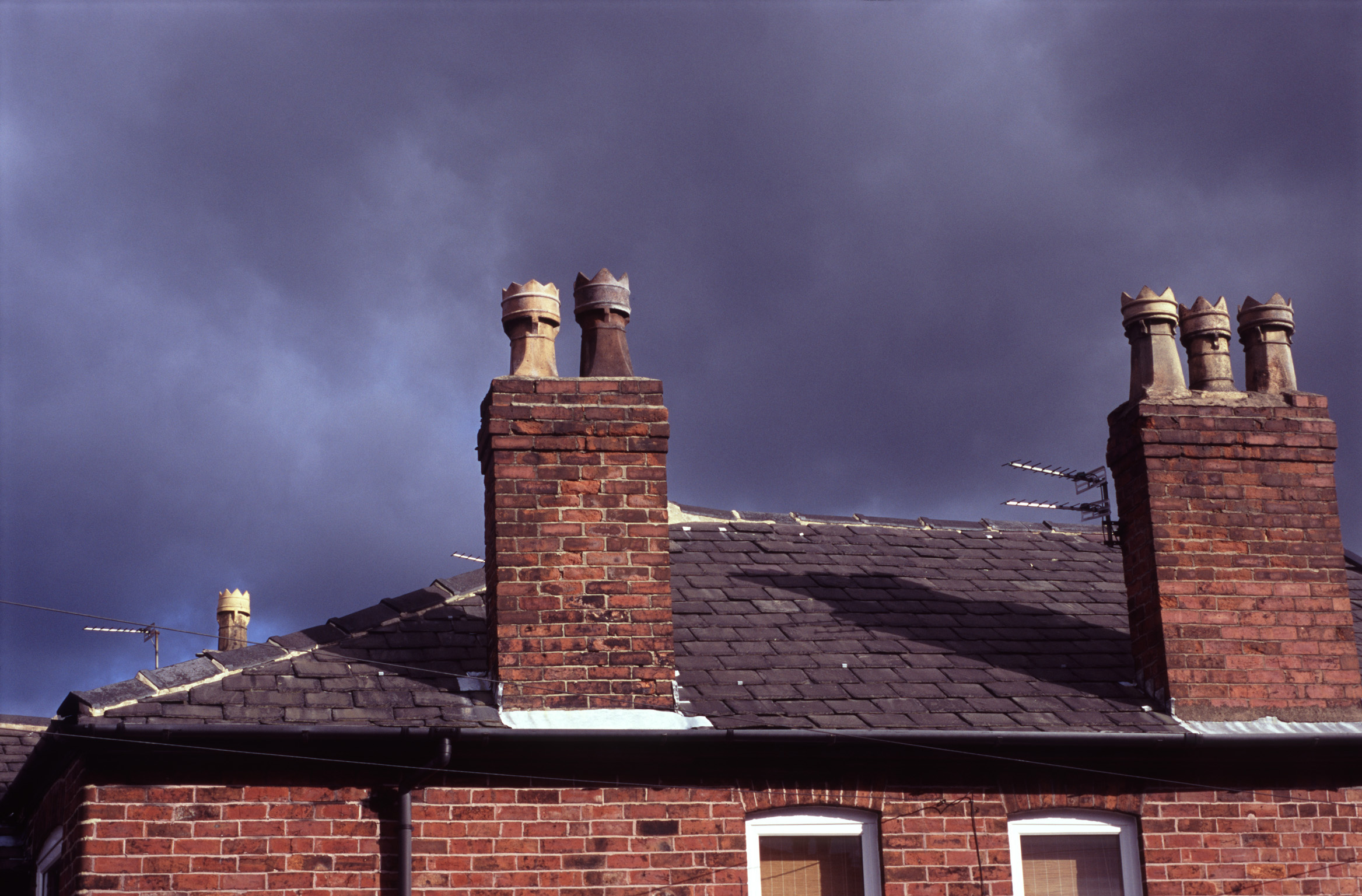 an image of Red brick chimney pots on old terraced houses in Stockport against an ominous cloudy sky