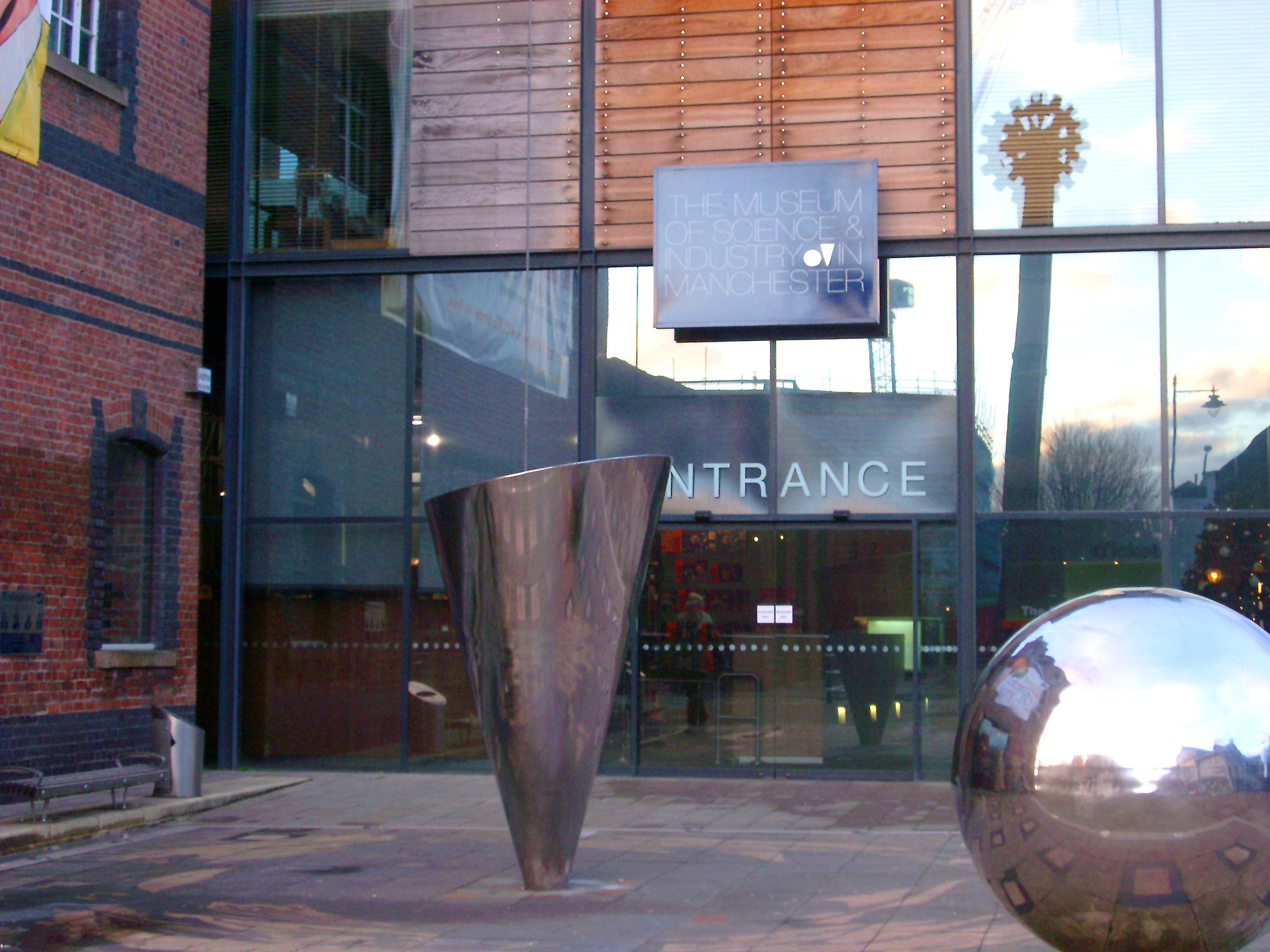 an image of Entrance to the Manchester Museum for science and industry with on outdoor sculpture of a shiny metal silver sphere
