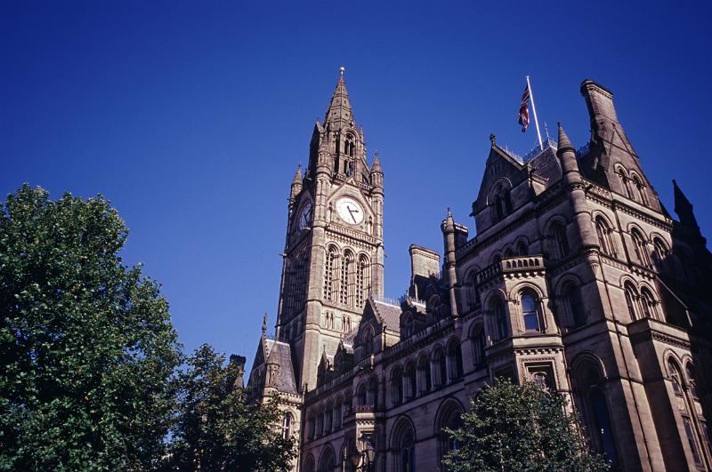 View of the exterior of the Manchester Town Hall with its Gothic revivaql architecture and ornate clock tower against a clear blue sunny sky