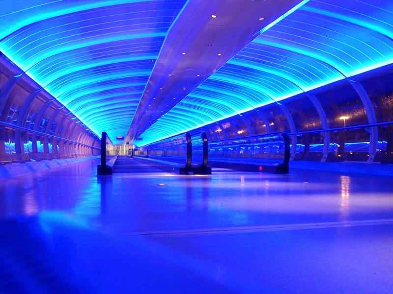 Interior of a blue airport sky bridge with travelators for pedestrians and overhead lighting in an arched ceiling