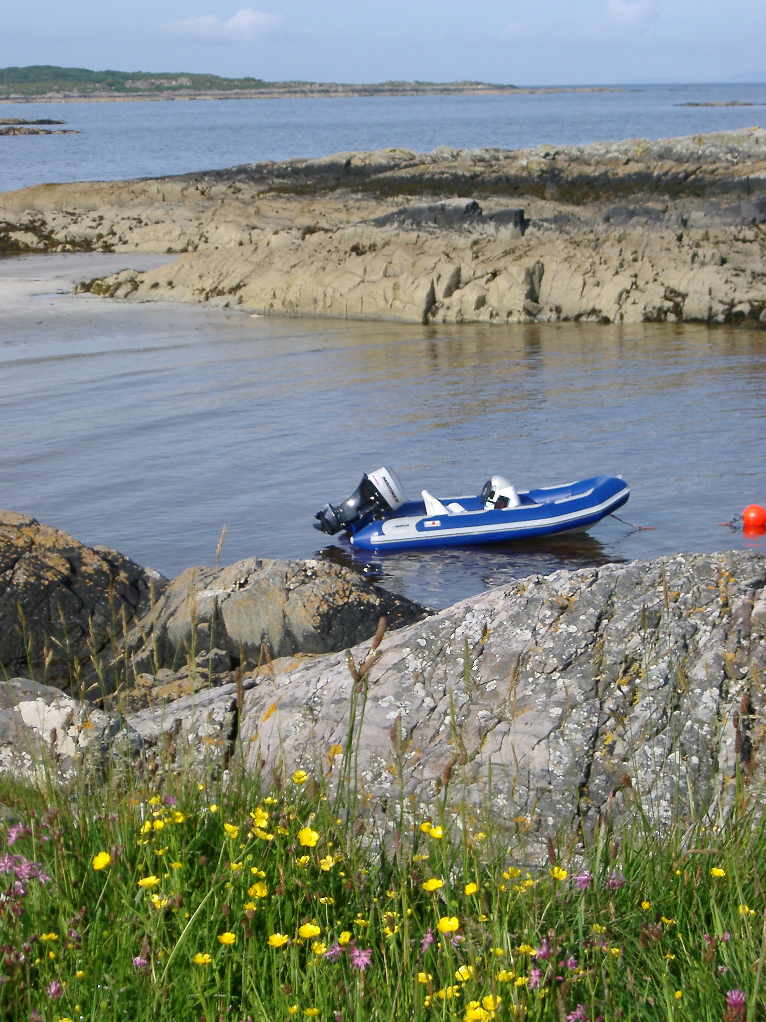 an image of Inflatable rubber dinghy with a small outboard engine moored to a buoy in a rocky coastal inlet in Maillag, Scotland