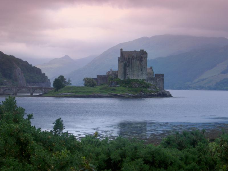 Scenic atmospheric panoramic view of Eilean Donan Castle, Scotland standing on its island in the centre of Loch Duich on a calm cloudy day with a feint mist and purple tint to the sky