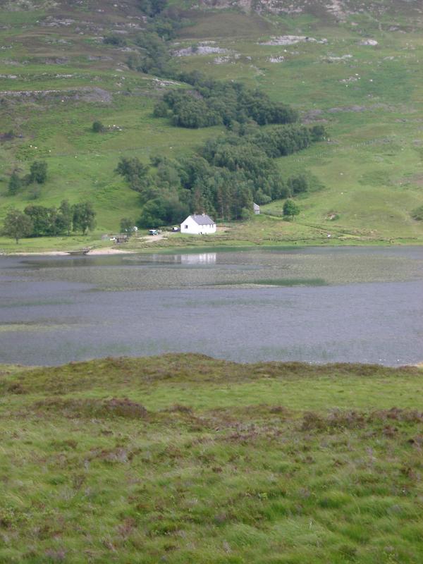 Distant view of a remote whitewashed house on the shores of loch in Scotland in a lush tranquil landscape