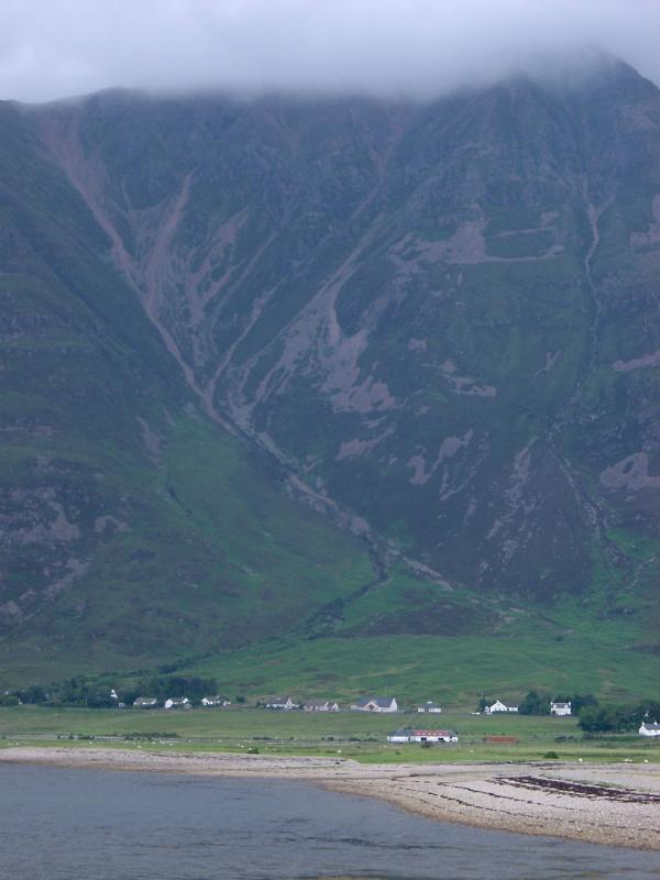 Scottish highlands landscape of a small settlement of houses around a sandy beach on the shores of a loch below a towering mountain peak shrouded in mist