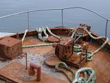 Rusty forecastle of a boat with a safety railing around the bow and old ropes and equipment on deck