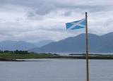 National flag of Scotland flying on a flagpole overlooking a placid loch on a cold cloudy day