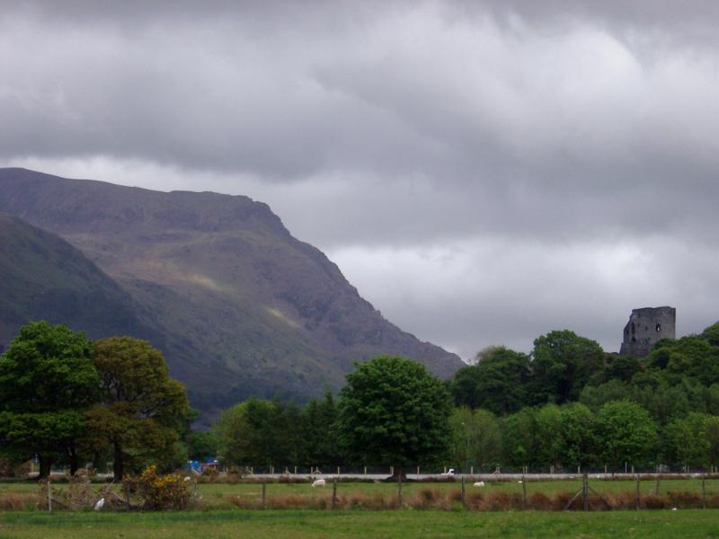 Welsh landscape with an old stone castle nestling amongst lush green trees at the foot of a mountain on a cold cloudy wet day