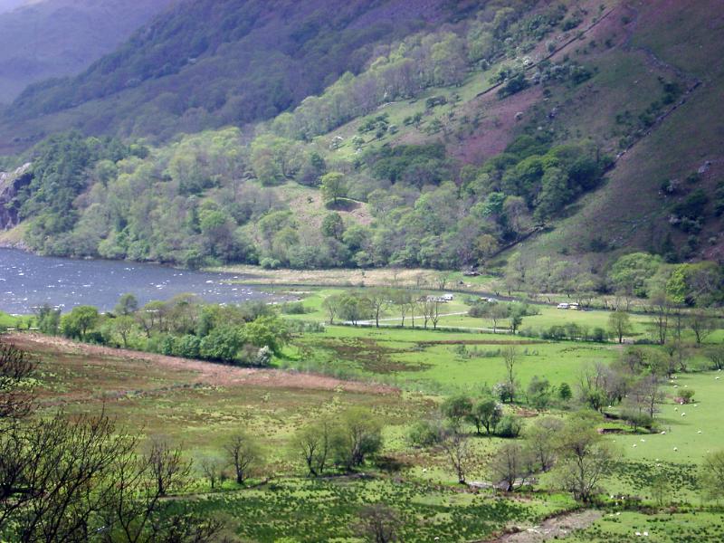 Lush valley with a farmhouse leading to a tranquil lake between steep mountains in Wales