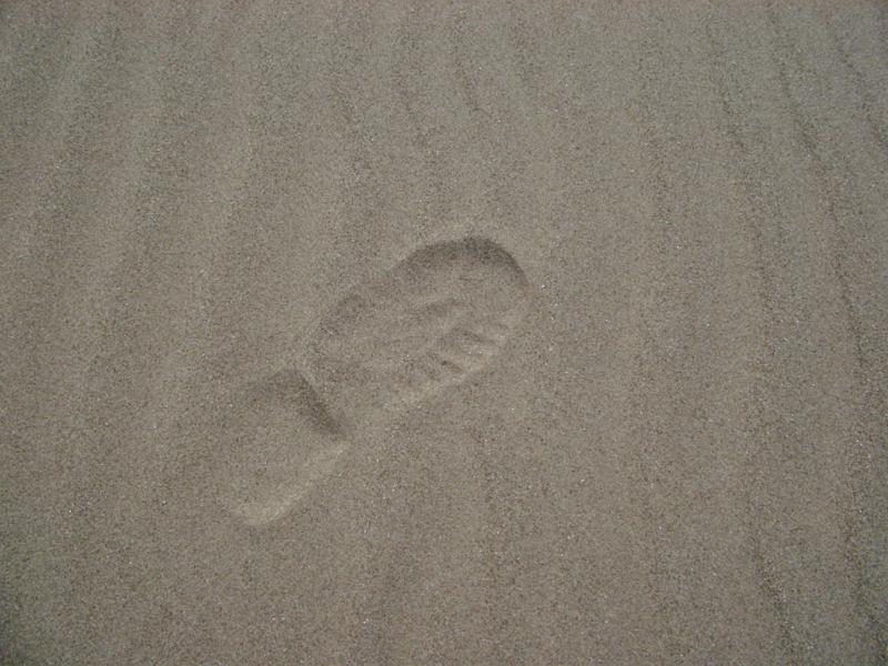 Close up shot of conceptual single human footprint on the gray sand at the beach.