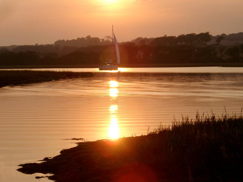 Yacht sailing on tranquil water at sunset passing through a bright orange beam of light reflected on the water