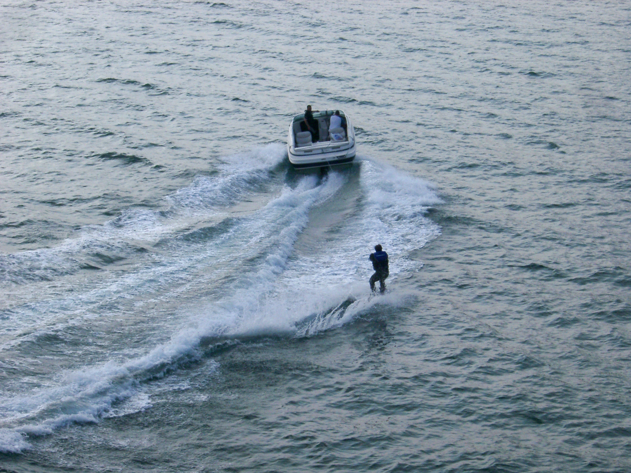 an image of High angle view of a speedboat and skier in a wetsuit speeding away from the camera in a depiction of extreme sport and outdoor activity
