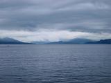 View over a calm ocean on a stormy overcast day of Scottish lochs and distant mountains
