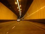 Covered road tunnel with two lanes of traffic traveling away from the camera on a curve lit by overhead central lighting