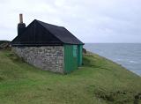 Stone shed or hut with a green facade on a headland overlooking the ocean providing shelter from the coastal weather