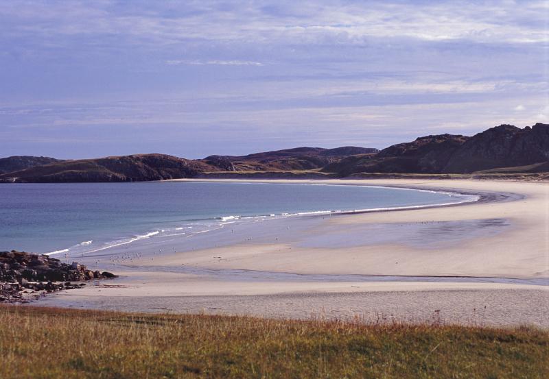 Sandy tranquil beach on the Isle of Lewis Sandy tranquil beach on the Isle of Lewis in the Hebrides with a curving shoreline and calm blue sea against a mountain backdrop
