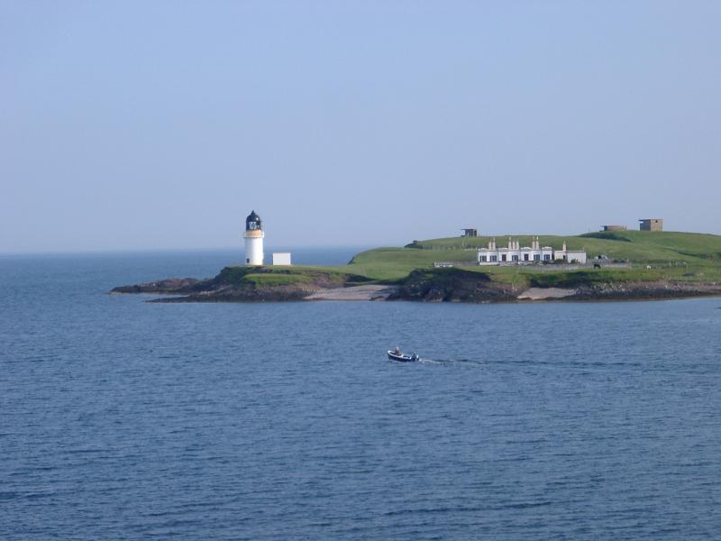 Scenic view across the sea of the headland with the Stornoway Lighthouse, Isle of Lewis, Scotland with a small boat passing by in the foreground