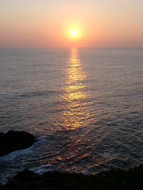 Serene scenic seascape with sun shining at the horizon and reflecting light on the surface of the sea, seen from the seashore, at twilight