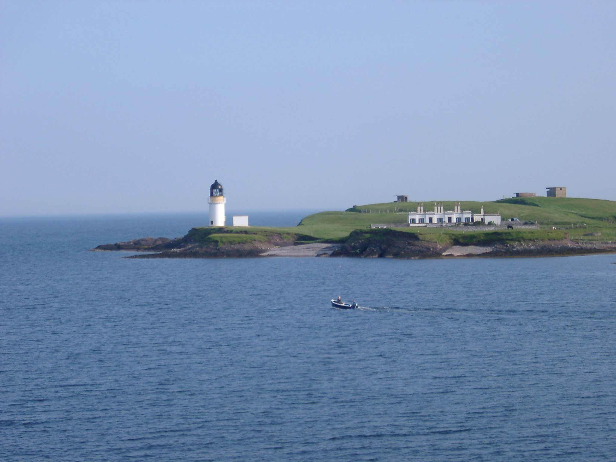an image of Scenic view across the sea of the headland with the Stornoway Lighthouse, Isle of Lewis, Scotland with a small boat passing by in the foreground