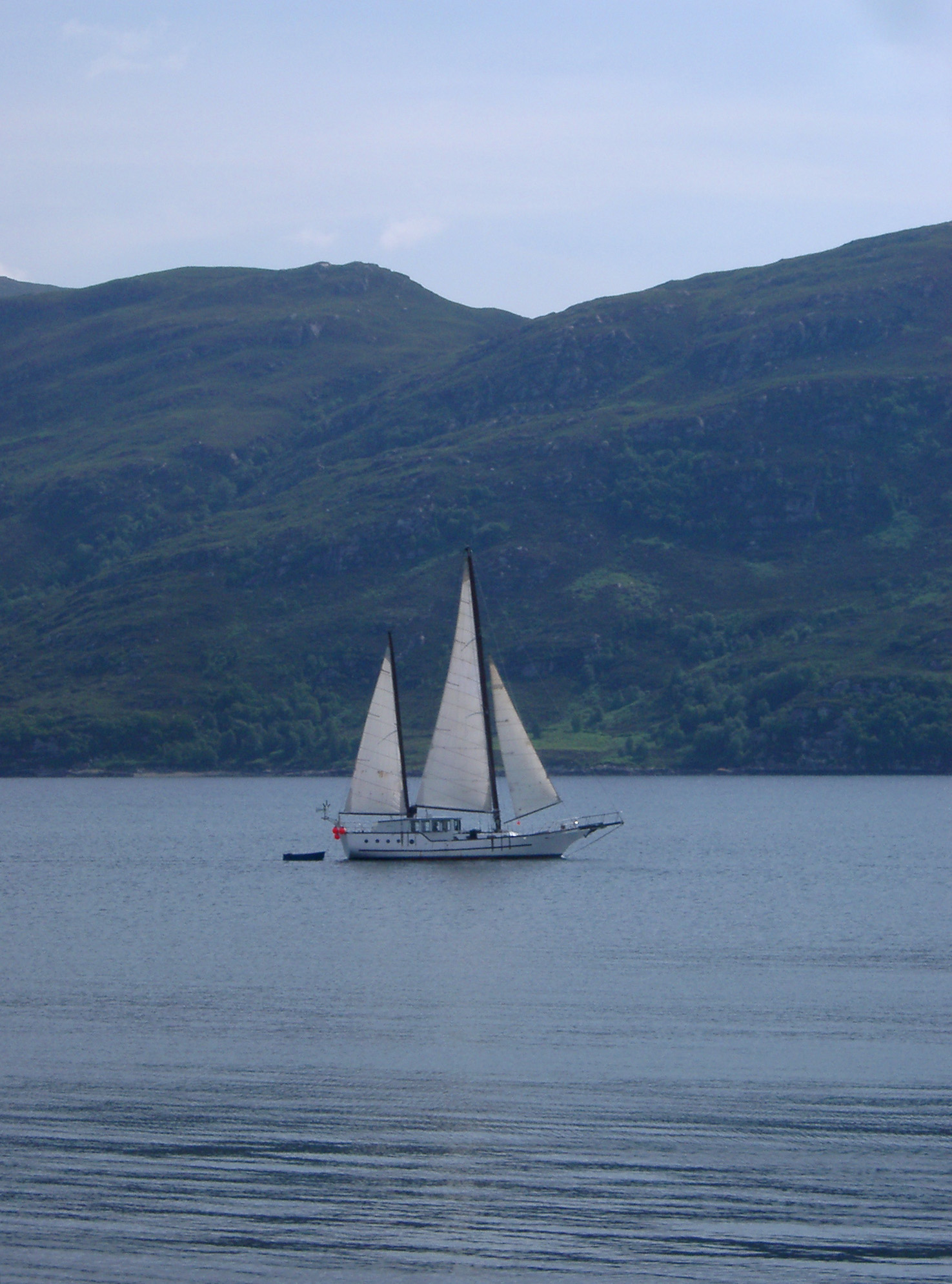an image of Sailboat Yacht Sailing on Scottish Loch on Overcast Day with Rolling Hills in Background