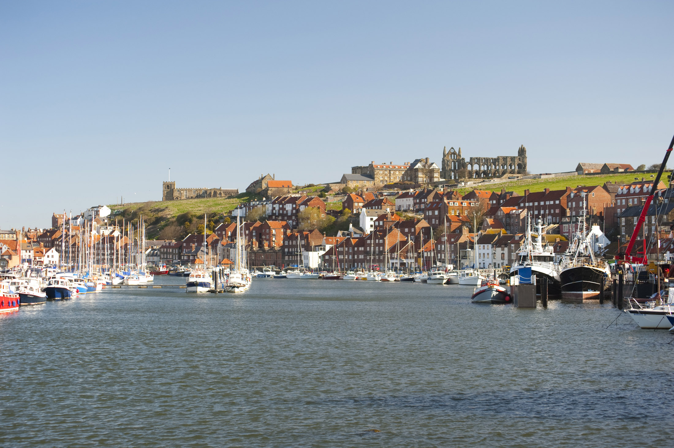 an image of the river esk flowing through the coastal town of whitby with the landmark abbey standing on top of the hill