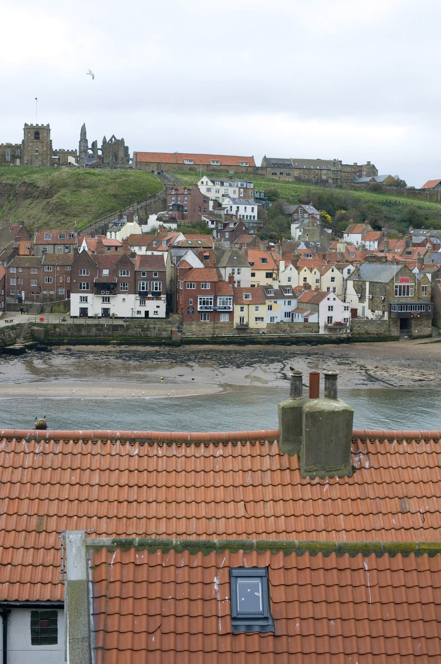 an image of looking over tiled cottage roof tops to the lower harbour and rows of cottages with the abbey and church on the hill