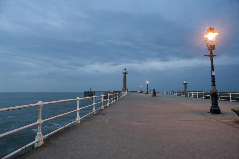whitby west pier looking along whitbys west pier after sunset lit by the warm glow of streetlights and the last light of the day
