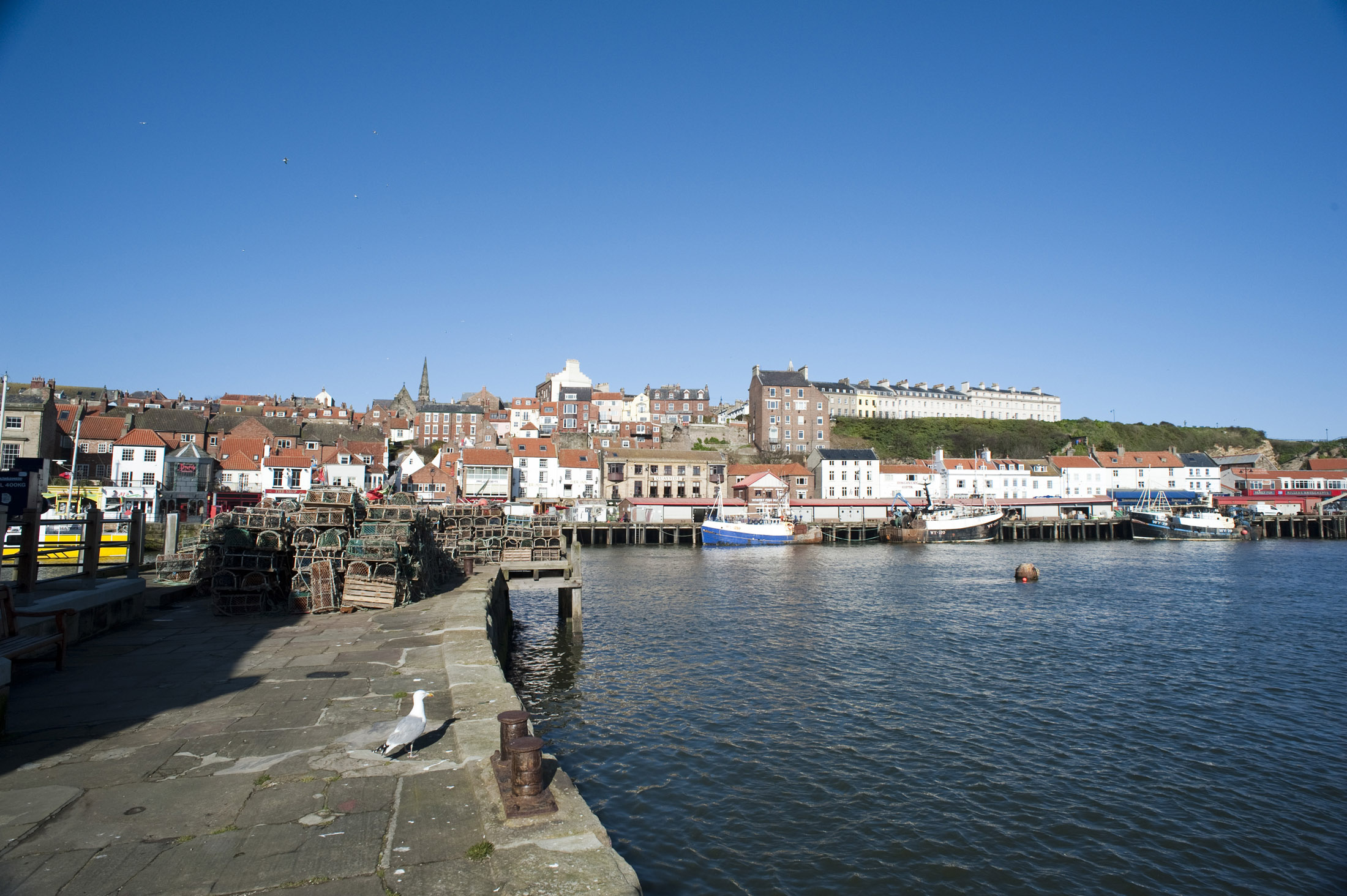 an image of lobster pots stacked on the tate hill stone pier with fishing boats docked at the fish market in the background