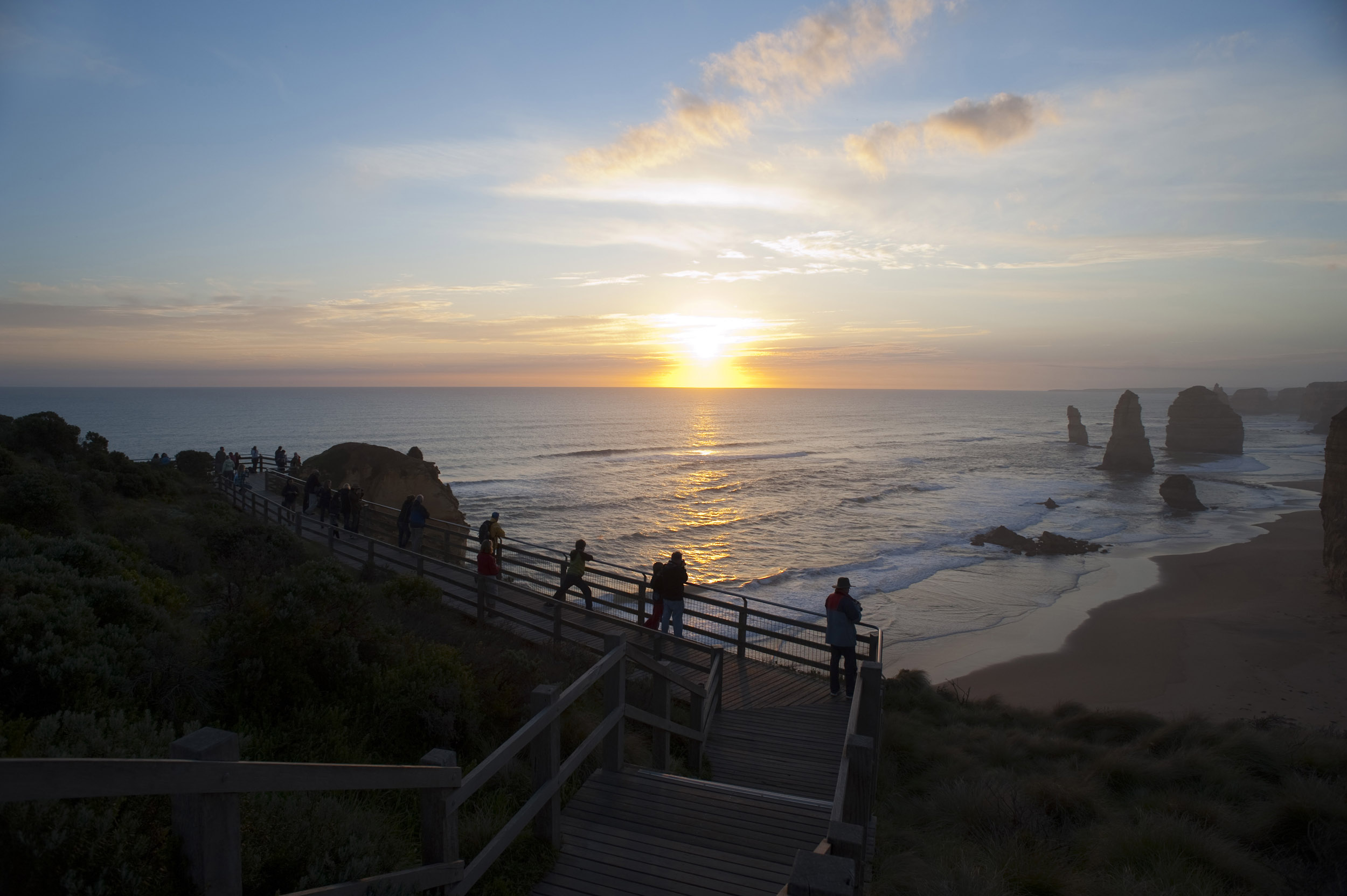 an image of A beautiful hazy sunset over the ocean, coastline, viewing platform and the 12 Apostles on the Great Ocean Road in Australia.