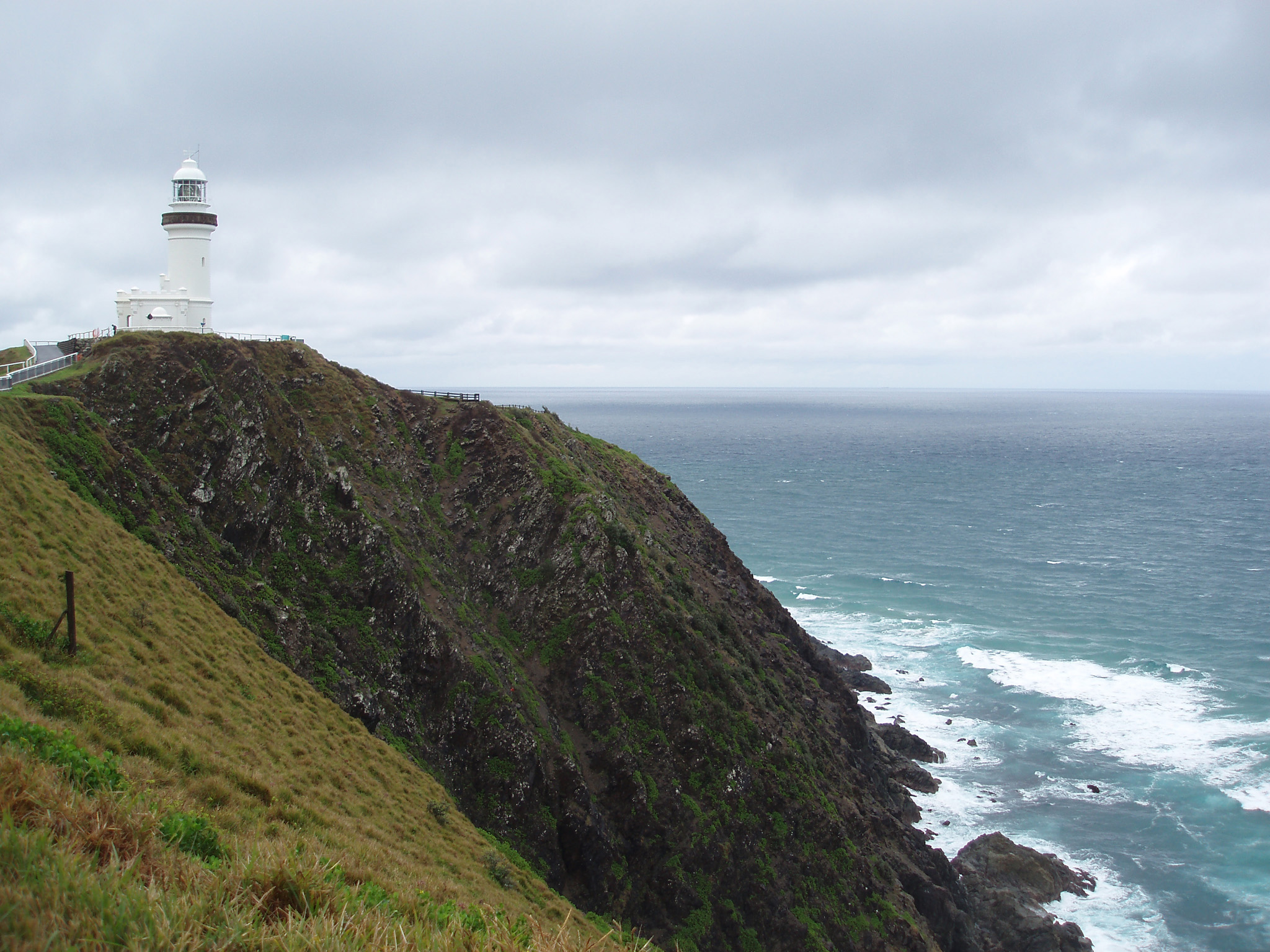 an image of Lighthouse at Grassy High Cliff at Beautiful Byron Bay in Australia on Light Gray Sky Above.