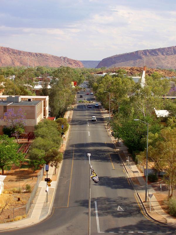 Aerial View of City Street in Australia with Green Trees on Sides and High Cliff in the distance