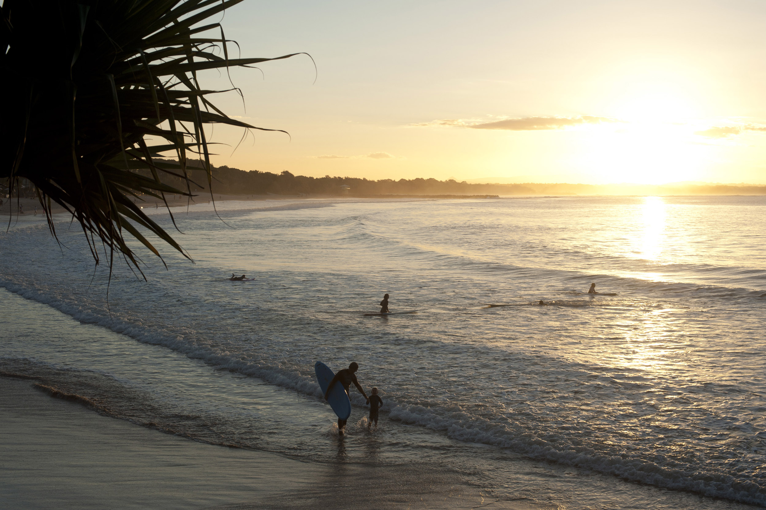 an image of Surfers in a calm ocean at Noosa, Australia at sunrise or sunset with the sun casting a golden path over the water